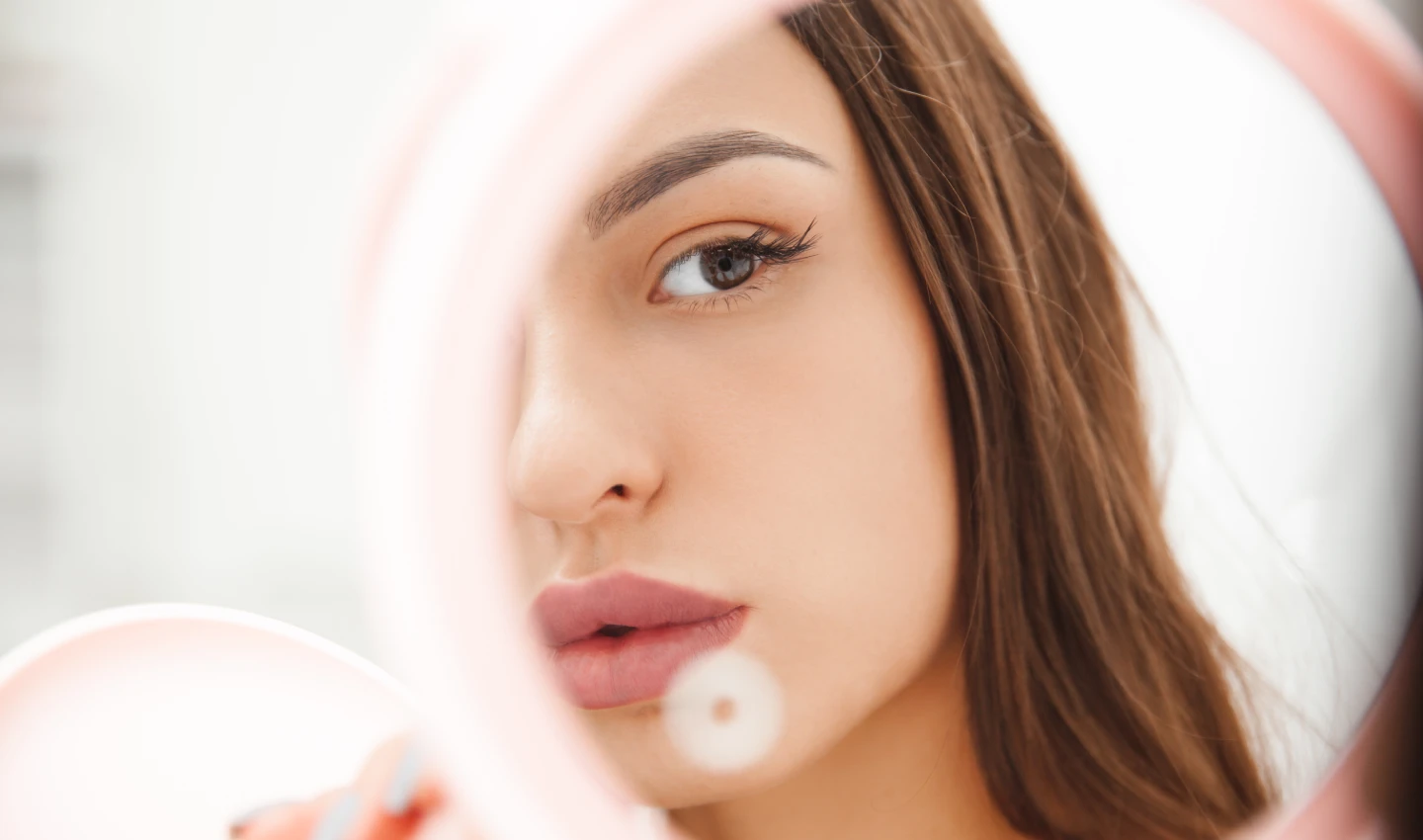 Woman looking at her blush in the mirror, demonstrating the power of long-lasting blushes for all-day radiance.