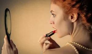 A woman applies bright red lipstick to her lips, demonstrating the use of statement lipsticks for prom and formal events.