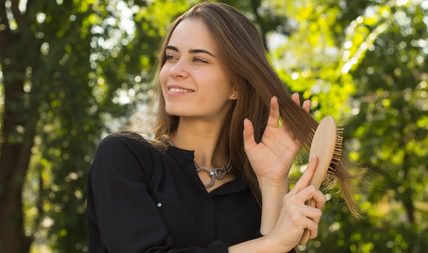 A young woman in a serene natural landscape, combing her hair with vegan hair care products.