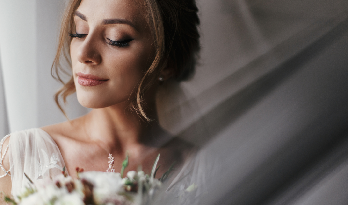 Minimal Natural Wedding Makeup: A stunning bride with a bouquet, posing at a window in soft light.