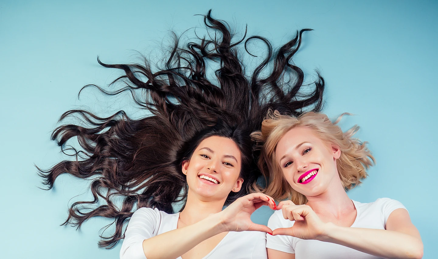 Two kind women with long hair and beautiful smiles lying down next to each other, promoting cruelty-free haircare.
