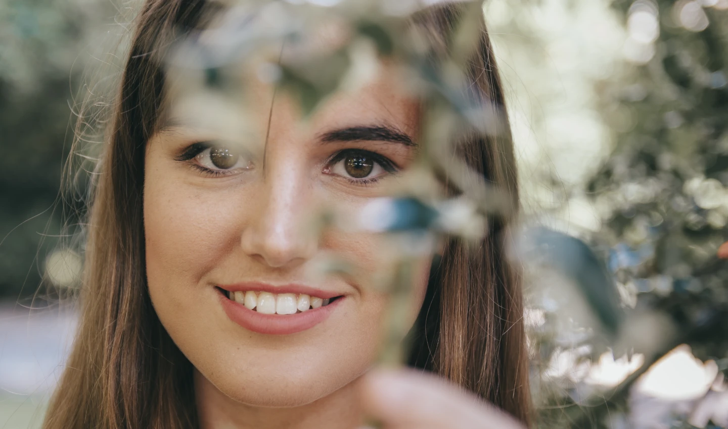 Perfect Natural Highlighting - Closeup shot of an attractive brunette girl behind the branches of the tree in the park