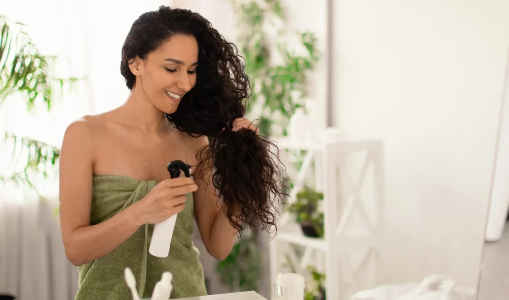 "Image of curly-haired handsome young Indian guy using leave-in conditioners for hair styling