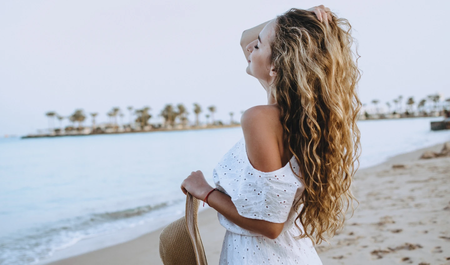 A young woman showcasing her radiant balayage hair, looking out over the sea, exemplifying the balayage hair trend in Australia