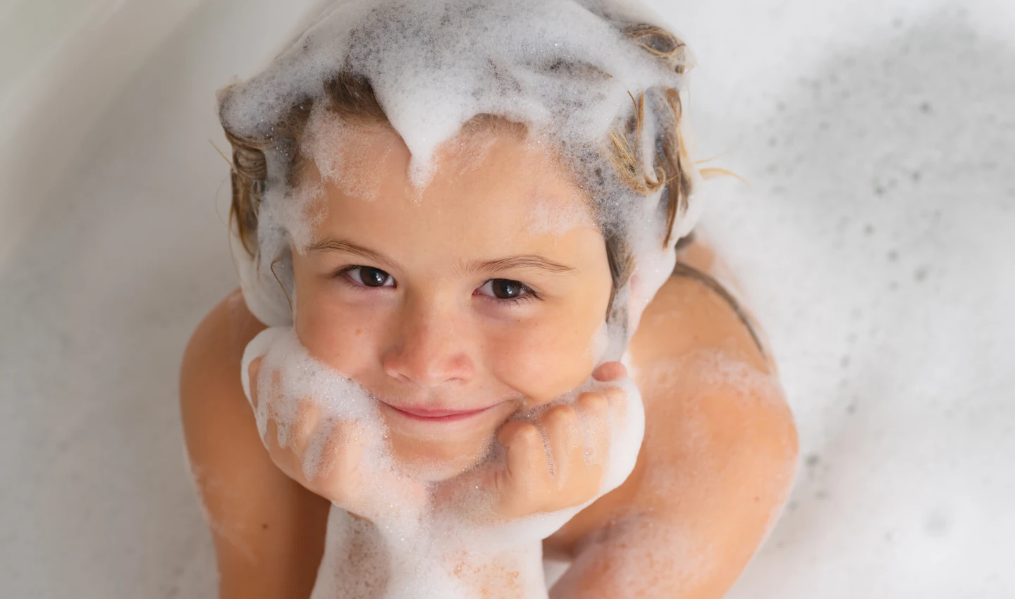 Child with shampoo foam and bubbles on hair enjoying a bath with Sulfate-Free Kids Shampoo