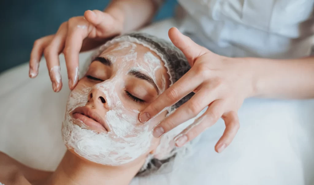 Closeup portrait of cosmetologist's hands applying exfoliating cleanser mask on client's face in a spa salon