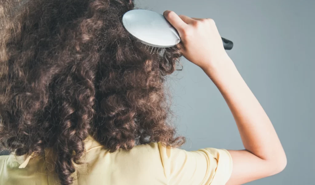 Closeup of a young woman with frizzy curly hair undergoing an eyebrow correction procedure in a beauty salon.