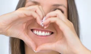 A woman with a radiant smile, holding heart-shaped hands near her mouth, showcasing her strong and healthy teeth, promoting sugar-free dental gums.