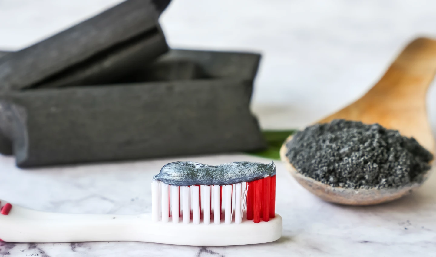 A toothbrush with charcoal toothpaste and charcoal in the background, representing charcoal-infused toothpastes.