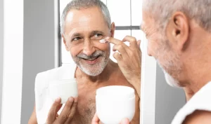 Close-up image of a senior man with a smile, applying Men's Anti-Aging Eye Creams