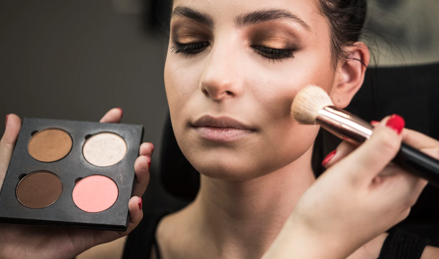 Beautiful model applying blush in a makeup studio - Perfect Blush Application