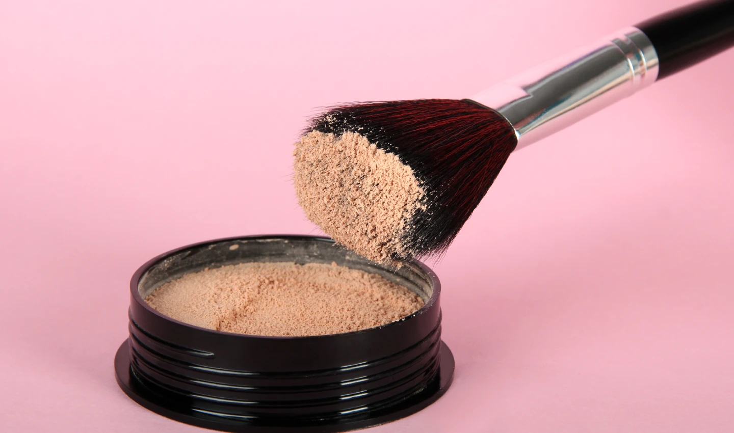 Setting Powder: A container of face powder with a makeup brush placed beside it