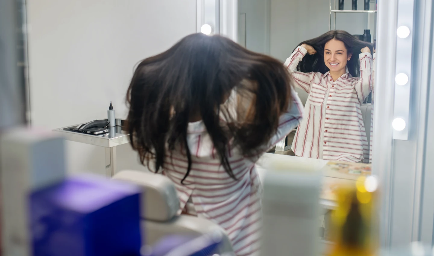 A long-haired young brunette looking in the mirror and doing her hair, dealing with greasy hair.