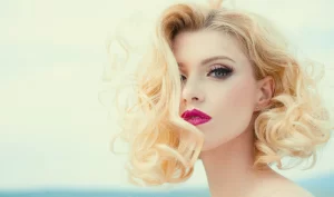 Closeup of a beautiful model with golden blond shiny wavy hair, showcasing a fashion haircut.