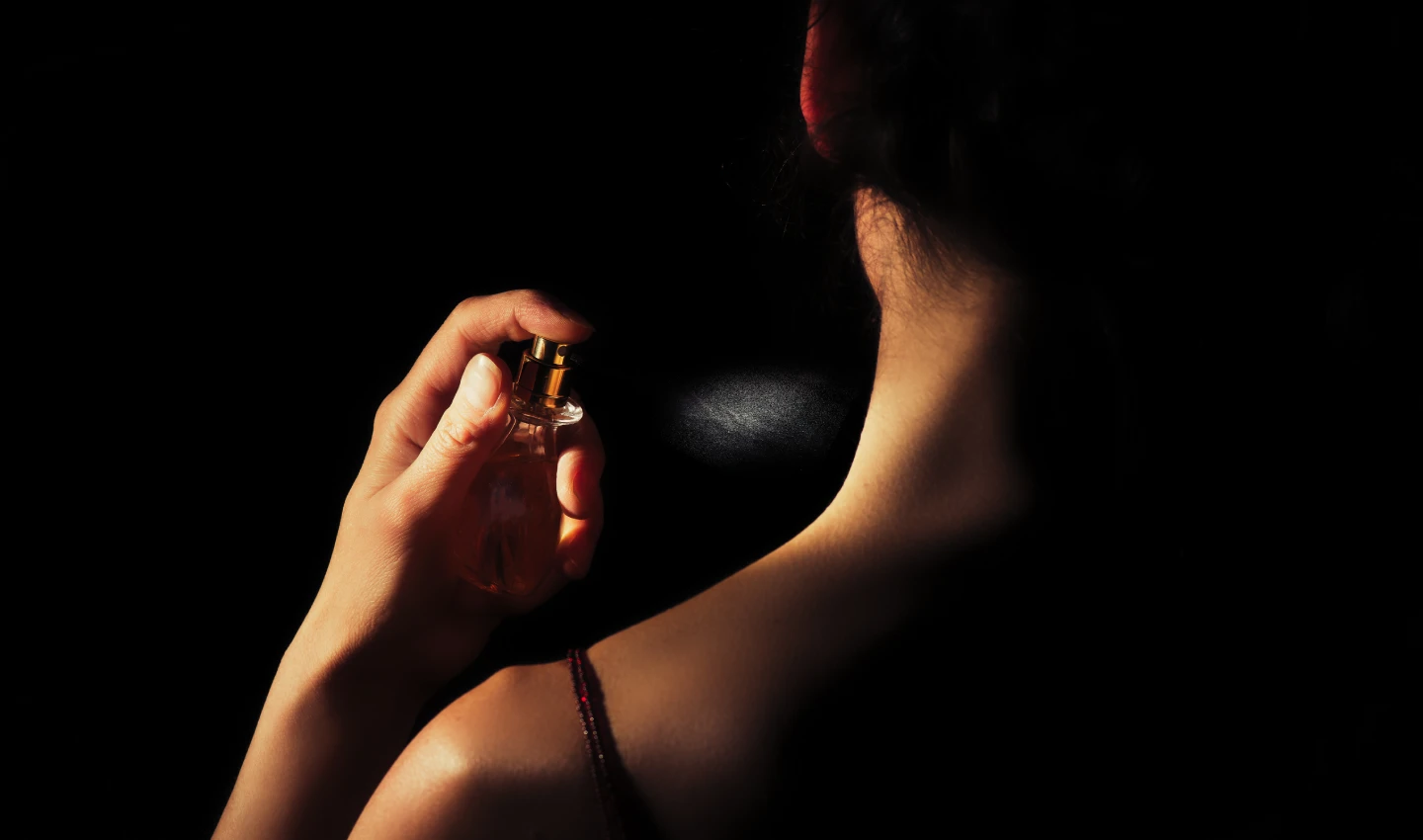A woman spraying perfume on her neck, exemplifying how scent plays a role in both personal and professional life.