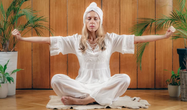 A stunning woman in great shape and with radiant skin practicing yoga in white robes.