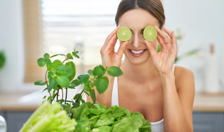 Woman playfully holding lime slices in front of her eyes, her radiant, youthful skin showcasing the anti-aging benefits of citrus