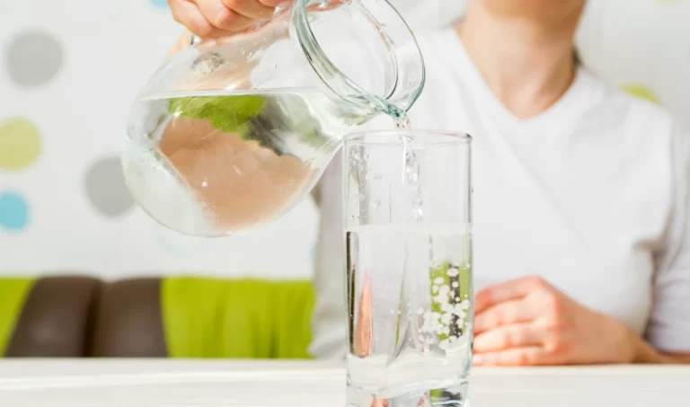 A woman pouring water from a jar into a glass, symbolizing the importance of hydration for healthy skin.