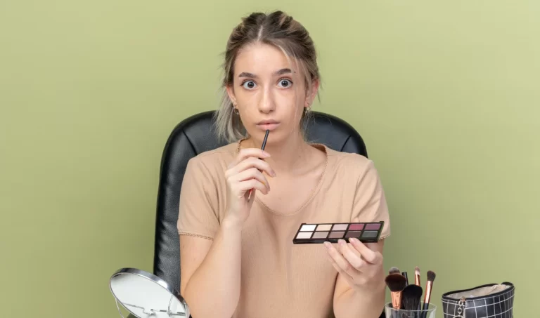 Attractive girl applying eye makeup while looking at the camera