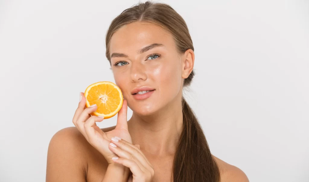 Attractive woman with even skin tone holding a slice of orange, symbolizing Vitamin C