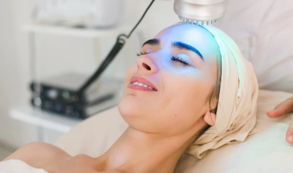 A woman relaxes with closed eyes while receiving LED therapy for even skin tone